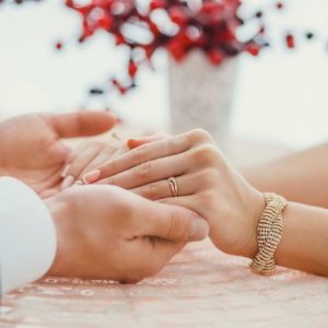 Unbeliever Dollar Photo groom holding bride's hands with ring at table